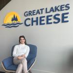 Shreya Mittal smiles in front of the Great Lakes Cheese sign
