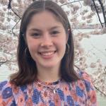 Katie Merritt smiles in front of a Cherry Blossom tree