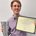 Tyler Holsopple smiles holding his first-place awards from the International Business Ethics and Sustainability Case Competition