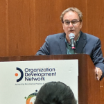 David Cooperrider stands at the podium at receiving OD Network International Conference