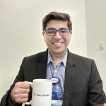 Anurag Virmani smiles while holding a MetroHealth coffee mug