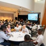 Crowd photo featuring incoming business school students sitting and chatting at a table during orientation