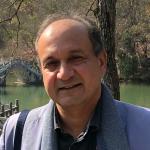 Photo of Alumnus Humayun Rashid wearing a gray suit in a scenic backdrop