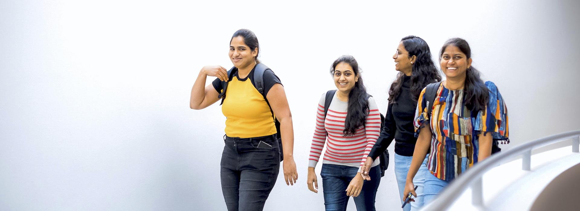 A group of femme students of color walk down hallway while smiling and laughing