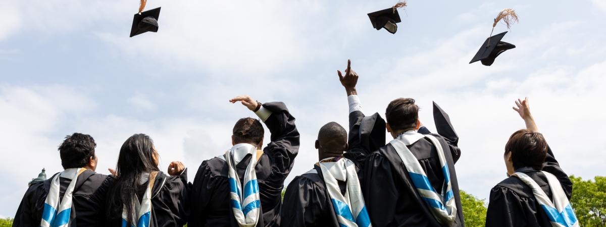 Six college graduates with their backs to the camera while throwing their graduation caps in the air