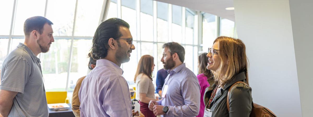 Attendees and mentors converse during a networking reception in a bright, modern room with large windows.