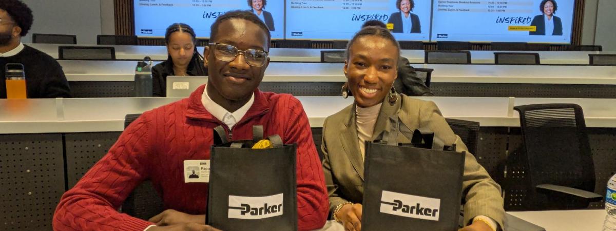2 students sitting together and smiling, each holding a bag