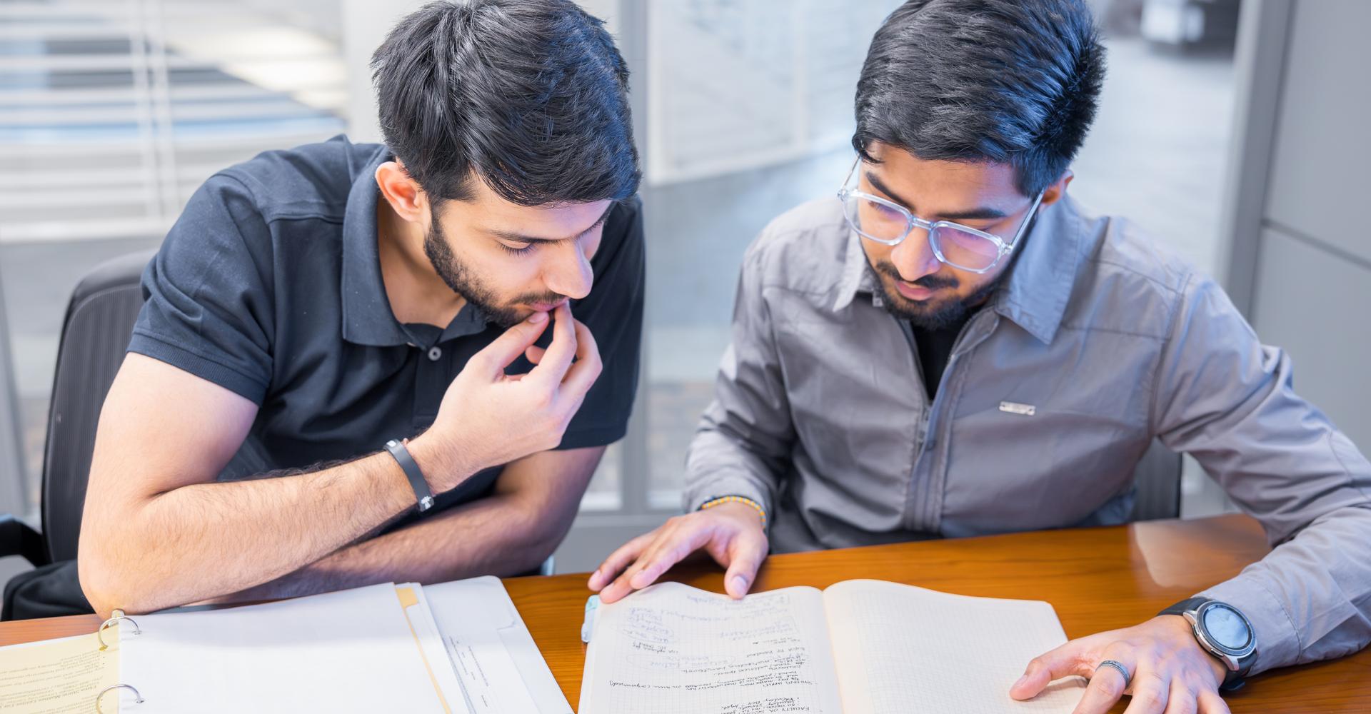 Two male students looking over notebooks sitting at a table