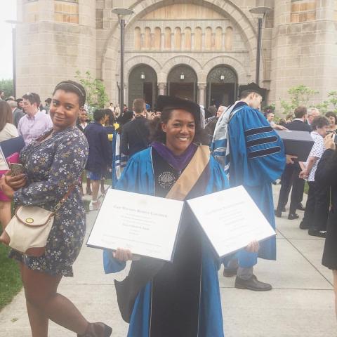 Bianca Smith poses with two degrees at a graduation ceremony wearing a cap and gown