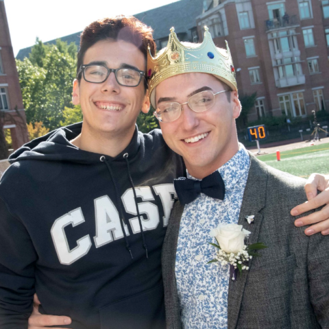 Photo of Adrian in a Homecoming crown and suit with another Case student in front of campus