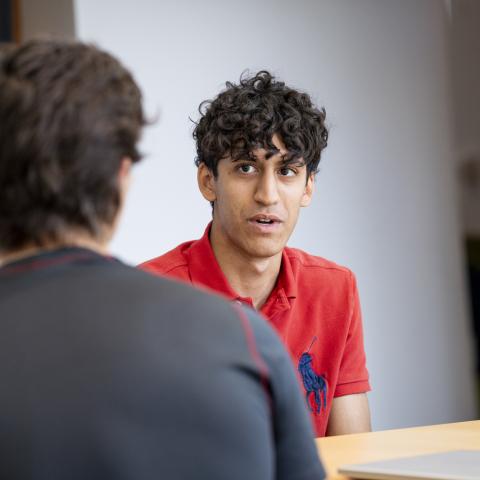 Student in a red shirt talking to another student in a classroom