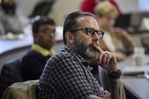 Close up of a white student with a beard and classes focusing intently on the professor