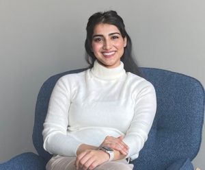 Shreya Mittal smiled in white turtleneck while sitting on a blue chair.