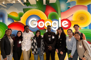 Students stand smiling in front of the sign at Google's offices in Silicon Valley