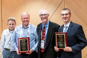 Group photo of four men, two holding plaques, during an annual accounting association meeting