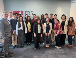 Group photo of more than a dozen students and several professors posing during a management conference