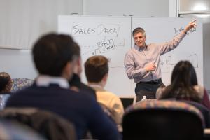 Faculty member teaches at the front of the classroom on a whiteboard.