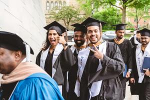 Student in graduation attire in an outdoor setting walking into commencement