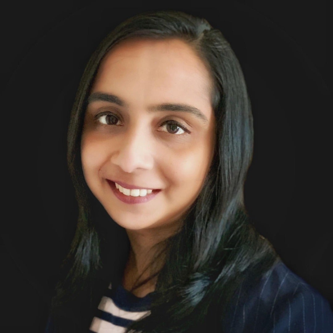 Bhadra Nair smiles in a headshot against a black background.