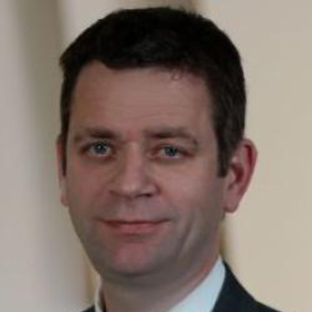 Simon Peck smiles in a suit.