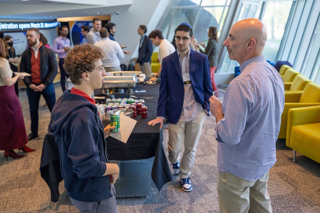 Attendees converse and mingle near a refreshment table during a networking reception at a university event.