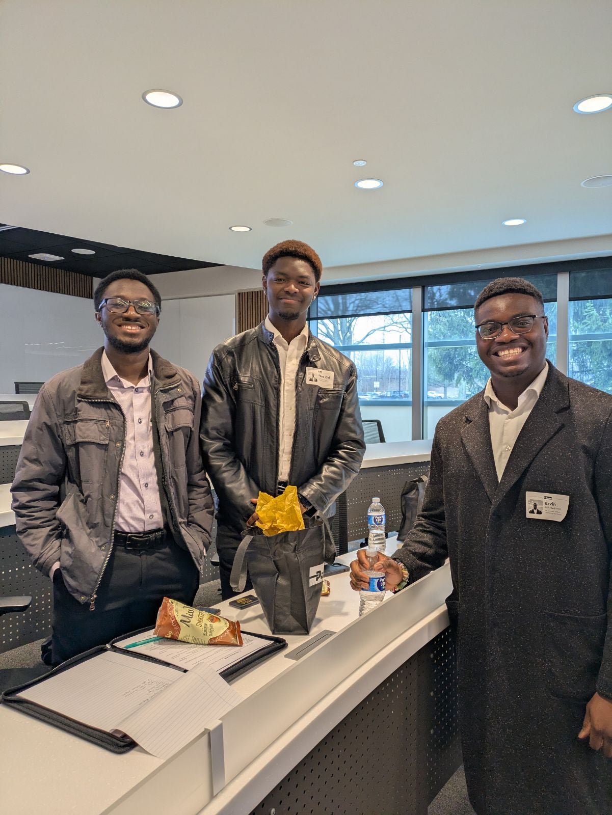 3 students smiling, standing over a table