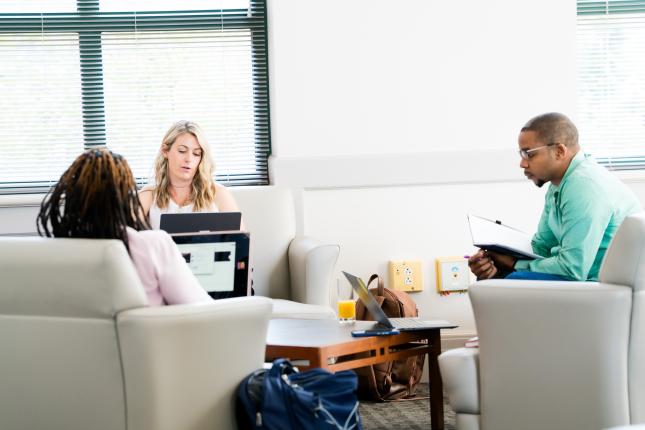 Three people sitting in a common area on their computers
