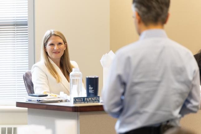 Cally Papenfus sitting at a desk speaking with a colleague