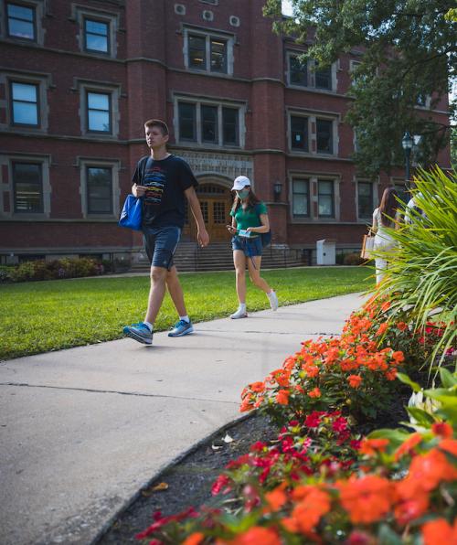 Students walk on a sidewalk on Case Western Reserve University's campus with flowers in the foreground.