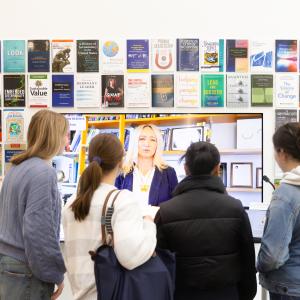 Four students standing in front of a television screen with a faculty avatar