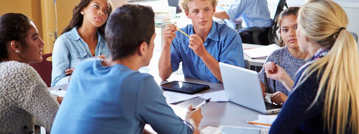 Students sitting in a group at a table with laptops. 