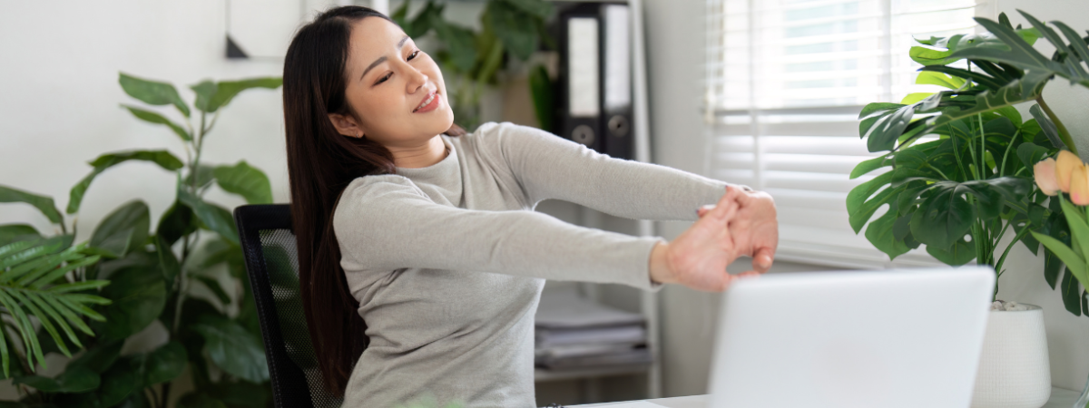 Person sitting in front of their laptop and stretching their arms with plants in the background