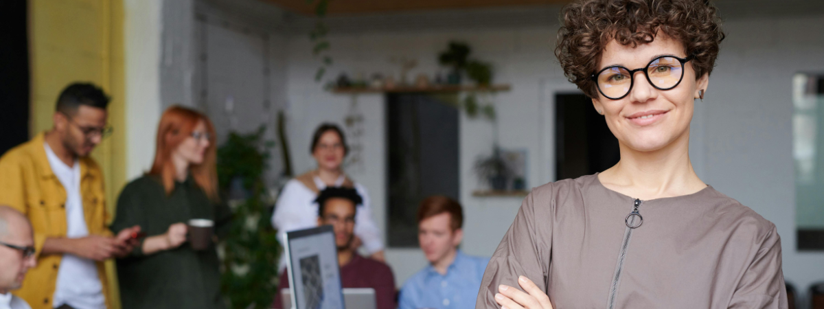 Photo of a person looking into the camera with their work team in the background