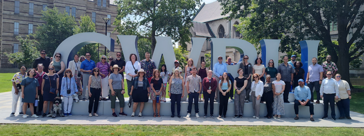 Photo of numerous faculty and staff in front of the large CWRU letters on the binary walkway
