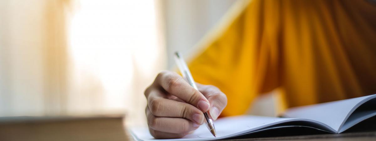 Student writing in a notebook with a pen