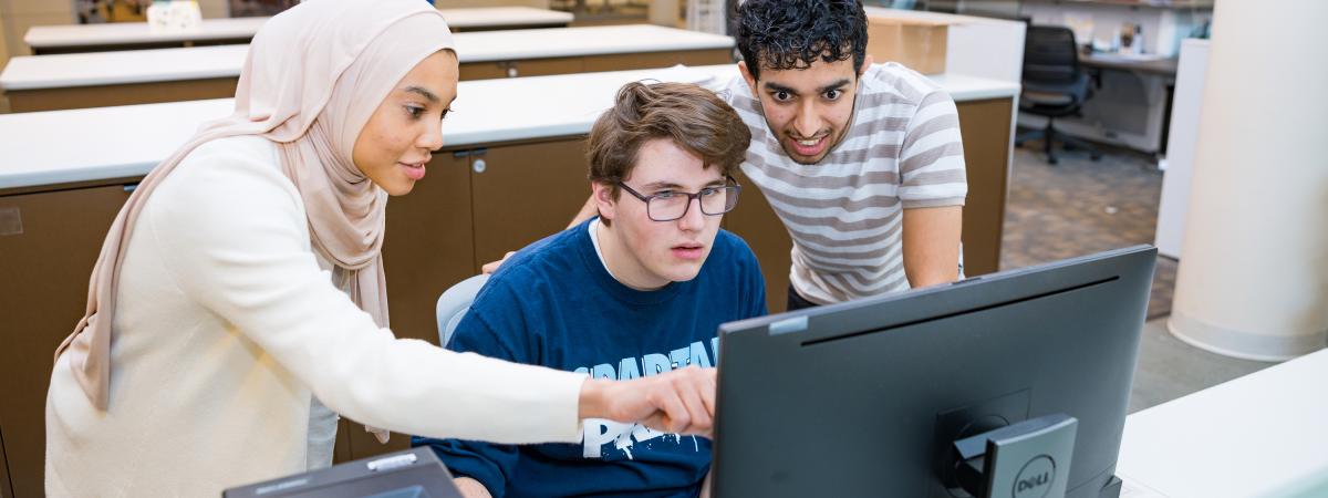 Three students collaborate at a computer.