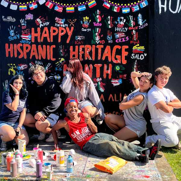 A group of six students pose in front of the CWRU spirit wall painted to say “Happy Hispanic Heritage Month.”