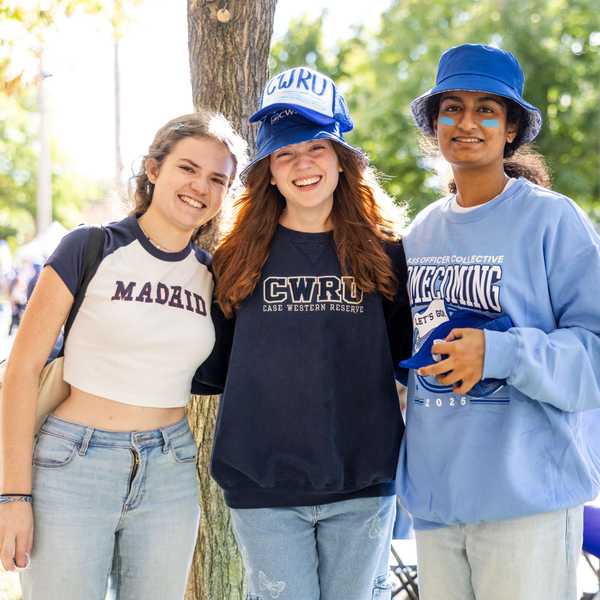 A group of three students in CWRU apparel pose outside smiling during homecoming.
